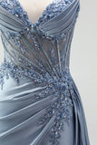 Robe de soirée gris bleu en satin avec un corset à strass, un effet de transparence et des fronces, à fines bretelles avec une fente
