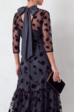 Robe invitée mariage midi noire coupe sirène, à col rond illusion, détails floraux, volants et manches 3/4
